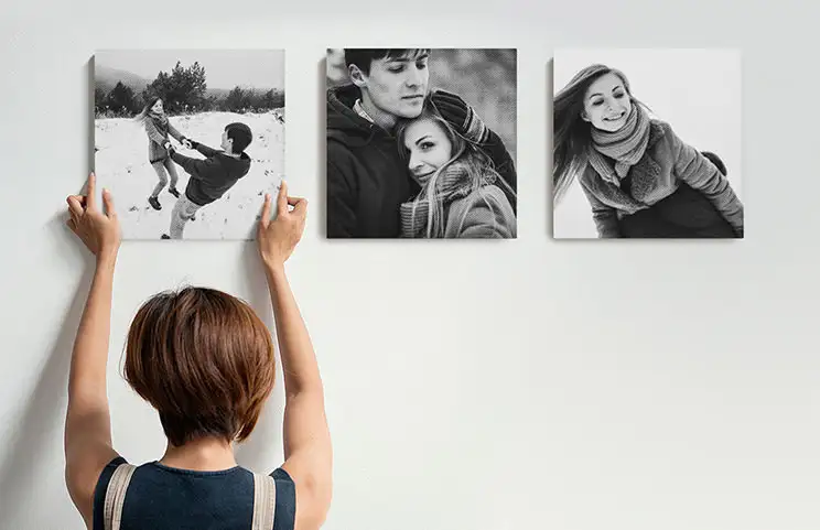 Frau hängt drei schwarz-weiße Familienfoto-Leinwände auf
