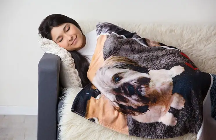 A woman wrapped in a personalised Printerpix Mink Touch blanket with a dog motif, happily sleeping on the sofa.