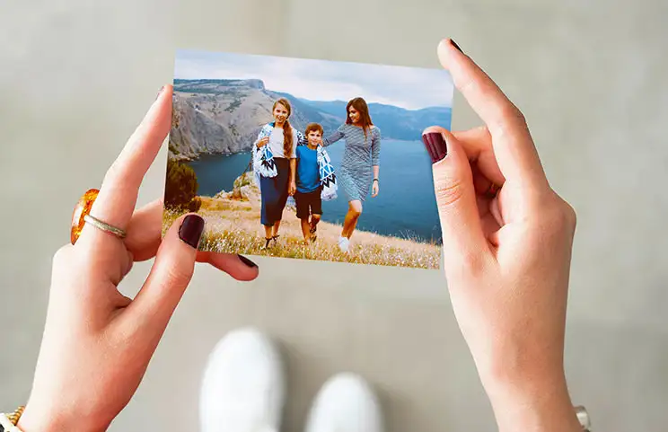 Hände halten einen Fotoabzug von drei Kindern im Urlaub