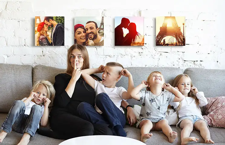 Mutter und vier kleine Kinder sitzen auf dem Sofa vor vier Foto-Leinwänden