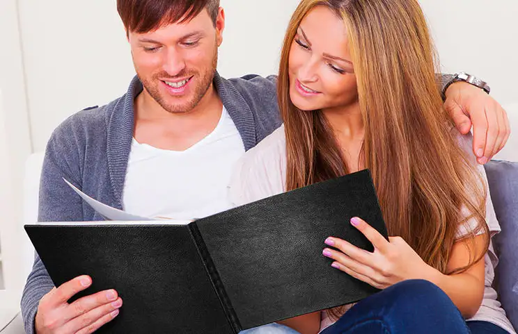 Paar betrachtet individuell gestaltetes Fotobuch mit Ledereinband von Printerpix