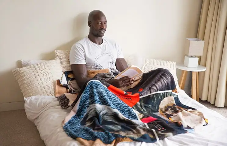 A man reading with a Printerpix photo blanket with a dog collage design over his lap.