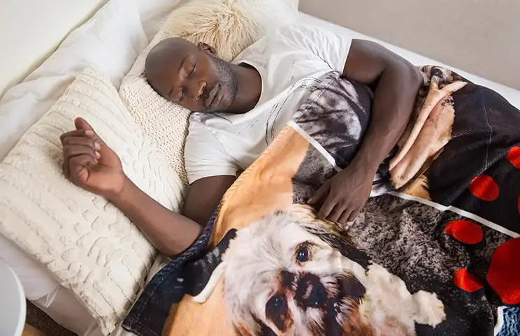 A man sleeping in bed under a personalised Printerpix blanket with a dog motif.